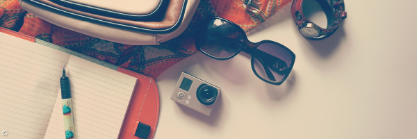 offenes Notizbuch, Kamera, Sonnenbrille und Tasche als Beispielbild für die Ferien
